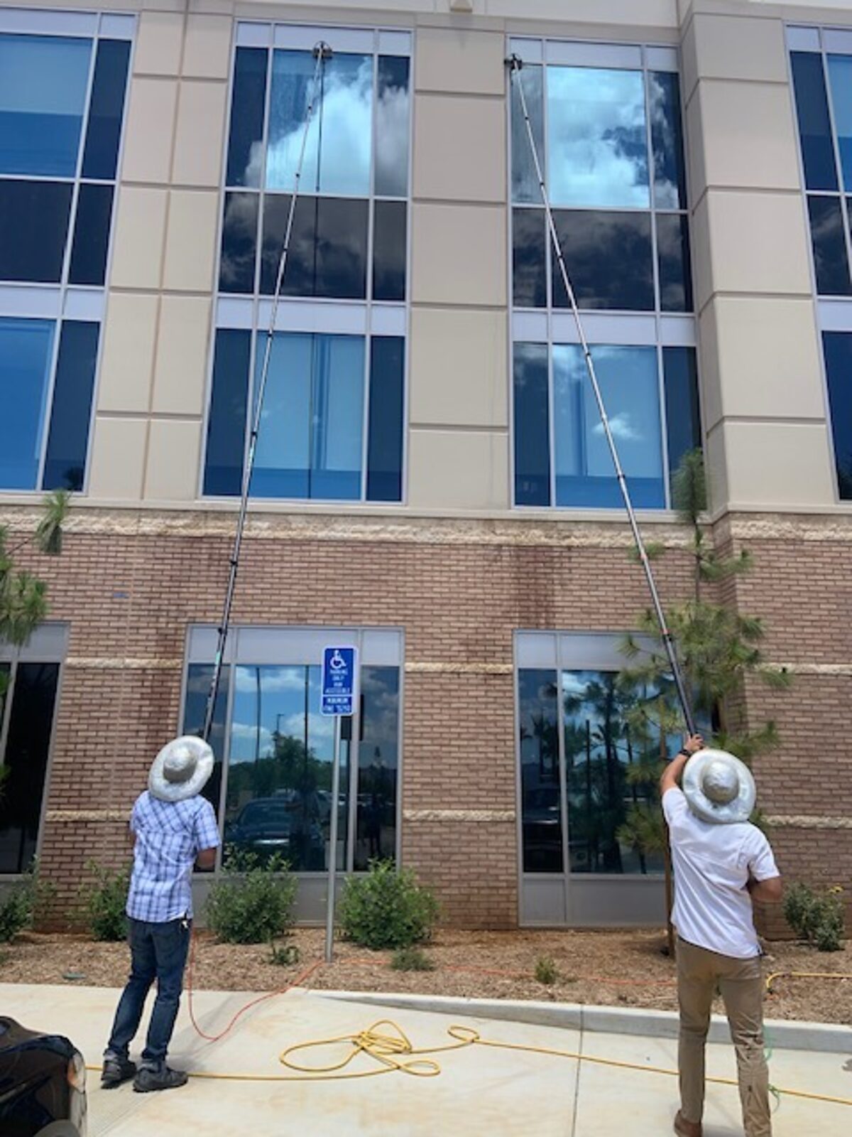 Two technicians on water-fed poles cleaning commercial glass