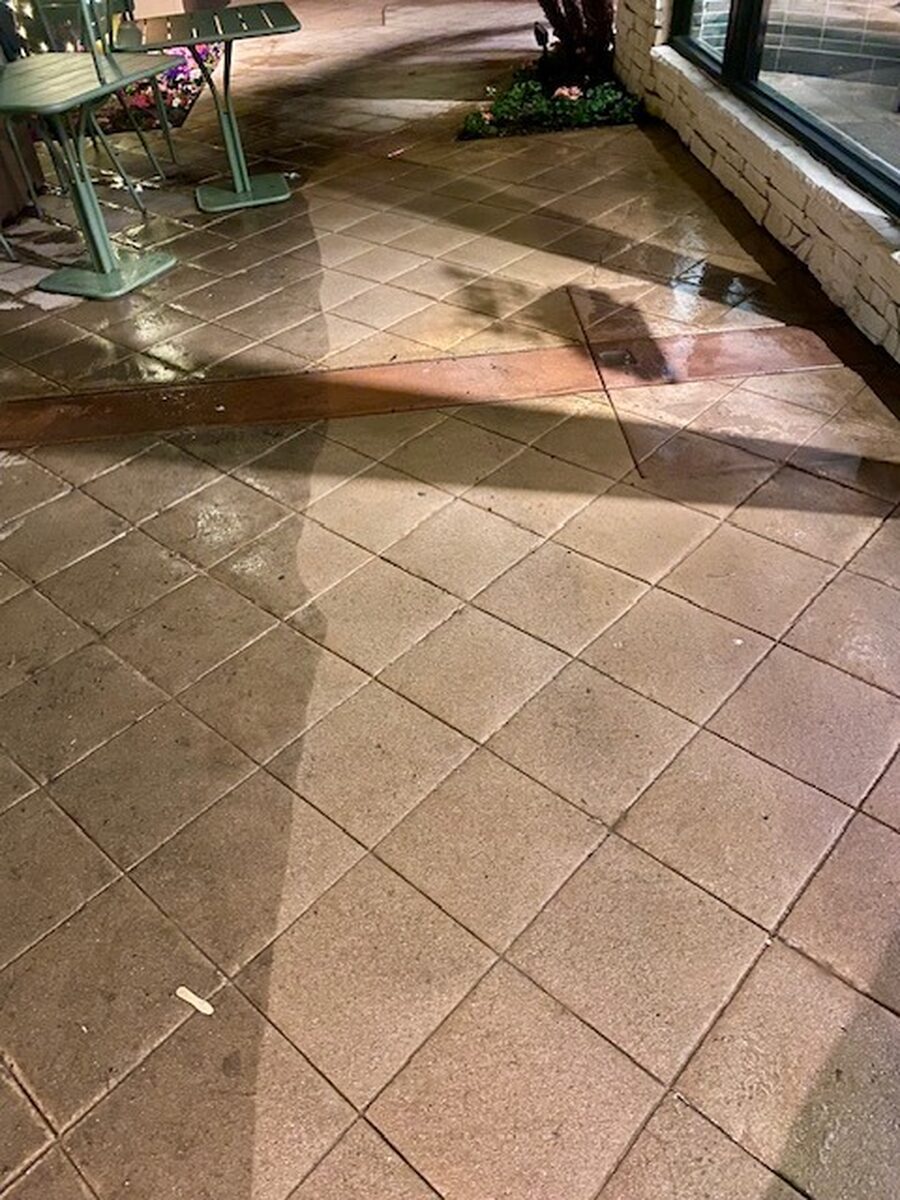 Wet patio pavers mid-wash, hose still out, the cleaned half darker than the dirty half
