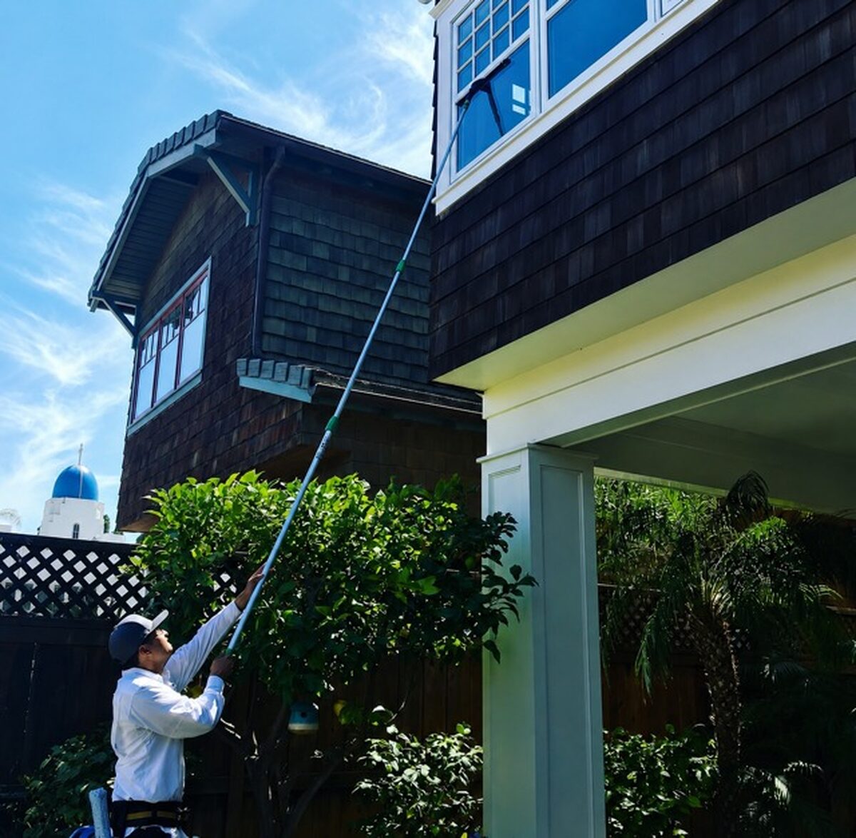 Technician on a water-fed pole at a two-story shingle house