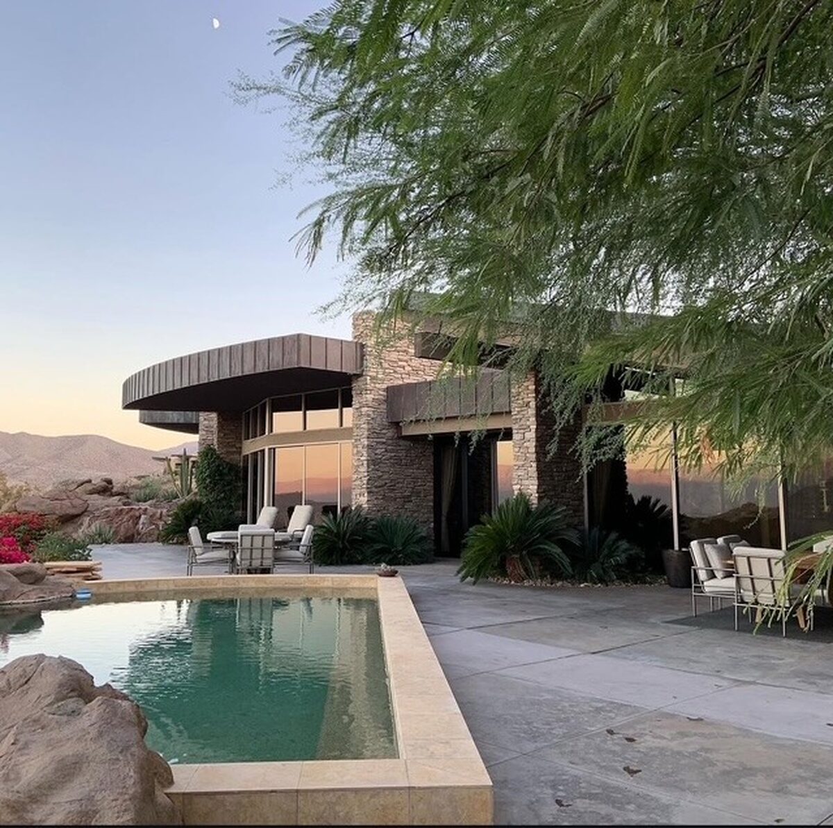 Desert-modern house and pool at dusk, glass lit from inside
